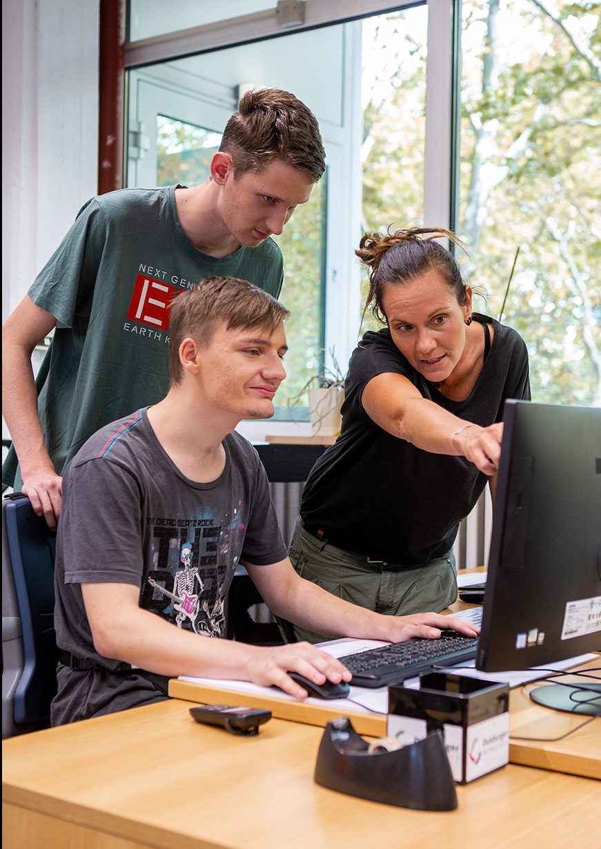 Gruppenleiterin erklärt Mitarbeitern am PC eine Aufgabe